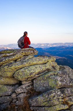 Erkek yürüyüşçü kaya oluşumları üzerinde otururken manzaranın keyfini çıkarır