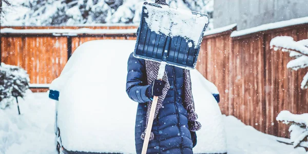 Kvinna med spade rengöring snö aeound bil. Vinter skotta. Re — Stockfoto