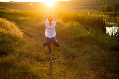 Gün batımında yoga yapan bir kadın göl kenarı farkındalığı ve akıl sağlığı nedeniyle poz veriyor.