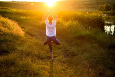 Gün batımında yoga yapan bir kadın göl kenarı farkındalığı ve akıl sağlığı nedeniyle poz veriyor.