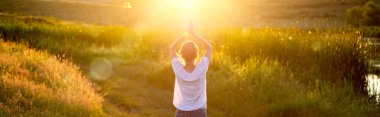 Gün batımında yoga yapan bir kadın göl kenarı farkındalığı ve akıl sağlığı nedeniyle poz veriyor.