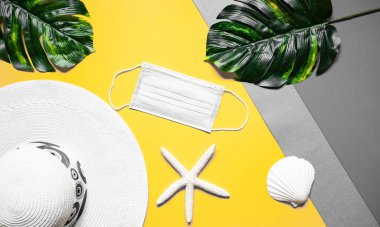 Düz renkli yaz arkaplanı, şapka kabukları mavi tıbbi maskeler - Coronavirus sırasında plaj tatili