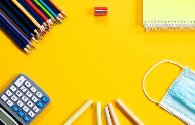 Okul konseptine dönelim. Okul gereçleri ve sarı arka planda tıbbi maske.