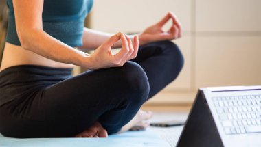 Evde yoga yapan bir kadın çevrimiçi video izliyor.