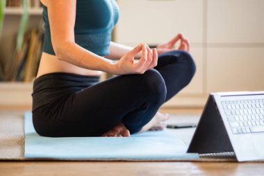 Evde yoga yapan bir kadın çevrimiçi video izliyor.