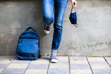 Okul çocuğu ayakları kot pantolonlu ve maskeli salgın sırasında okula geri dönüyor.