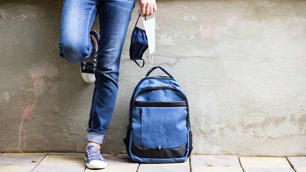 school kid feet in jeans backpack and mask back to school during pandemic