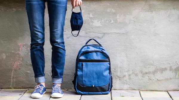 school kid feet in jeans backpack and mask back to school during pandemic