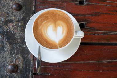 Kalp şeklinde köpük ahşap masa arka plan üzerinde beyaz bir fincan CAPUCINO veya sütlü kahve