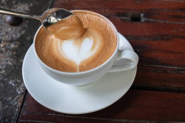 Kalp şeklinde köpük ahşap masa arka plan üzerinde beyaz bir fincan CAPUCINO veya sütlü kahve