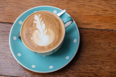 Kalp şeklinde köpük ahşap masa arka plan üzerinde beyaz bir fincan CAPUCINO veya sütlü kahve