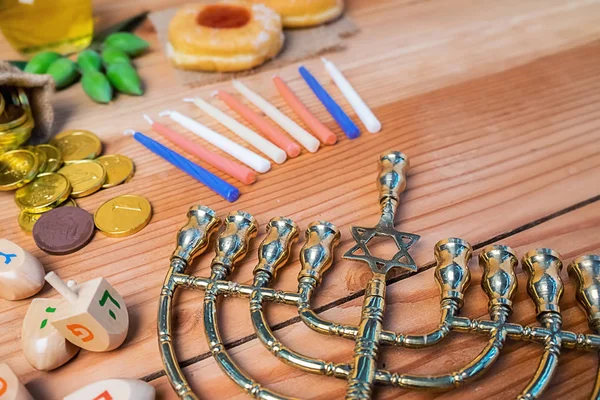 Top view of jewish holiday hanukkah celebration with menorah (traditional candelabra), wooden dreidels (spinning top), donut, olive oil and chocolate coins on wooden table.