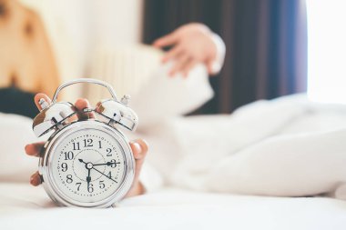 Tahriş olmuş genç kadın kapalı koyarak onu çalar saat sabah yumuşak sabah ışık ile. Rahatlatıcı kavramı.