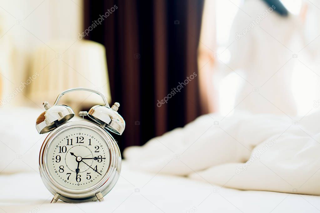 Alarm clock standing on bedside table has already rung early morning to wake up woman is stretching in bed in background.Relaxing concept.