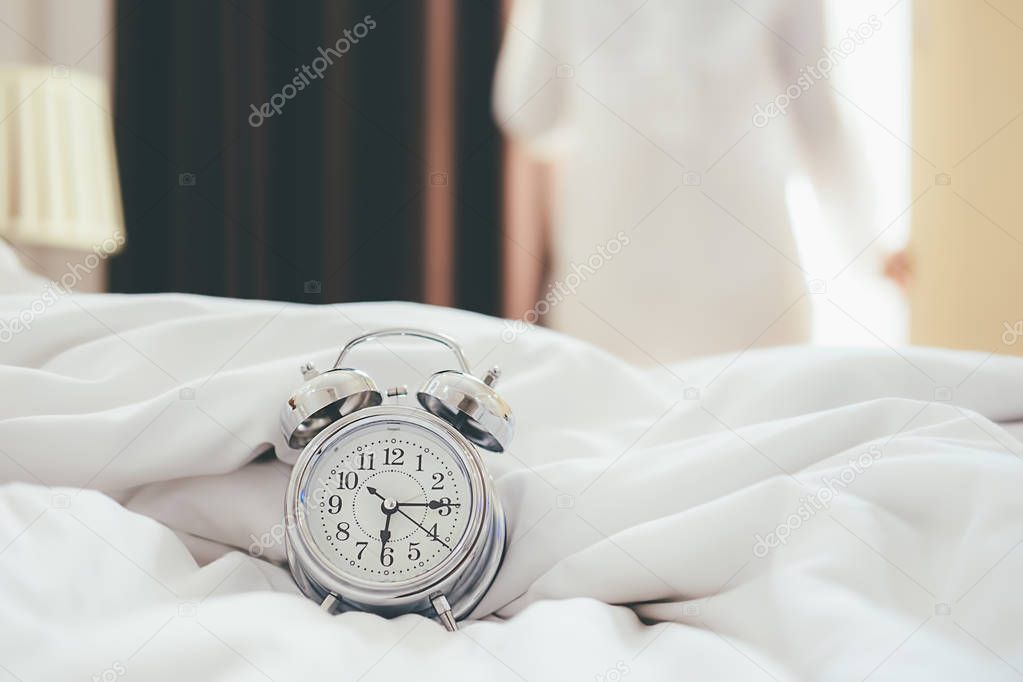 Alarm clock standing on bedside table has already rung early morning to wake up woman is stretching in bed in background.Relaxing concept.