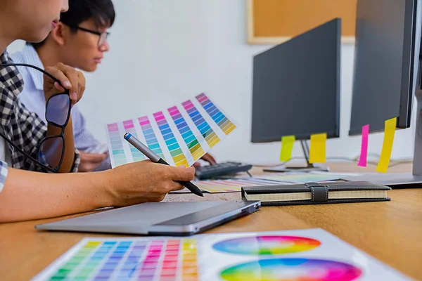 Graphic design with color swatches and tablet on a desk. Graphic designer drawing something on tablet at the office with work tools and accessories.