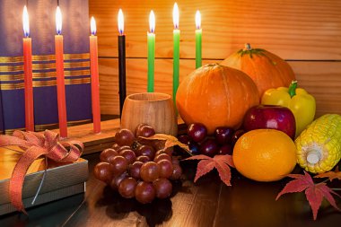 Kwanzaa holiday concept with decorate seven candles red, black and green, gift box, pumpkin,corn and fruit on wooden desk and background. clipart