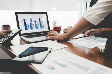 Kafesinde çalışan ve dizüstü bilgisayar kullanan genç iş adamlarının başarılı takım çalışmalarının sonuçlarını gösteren çizelge ve grafikleri ellerinde tuttukları düşünülürse....
