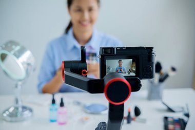 Kadın dijital kamera kullanarak kozmetik üzerine blogu için video çekiyor. Genç bayan blogcu elinde kozmetik malzemelerle kamera ekranında.