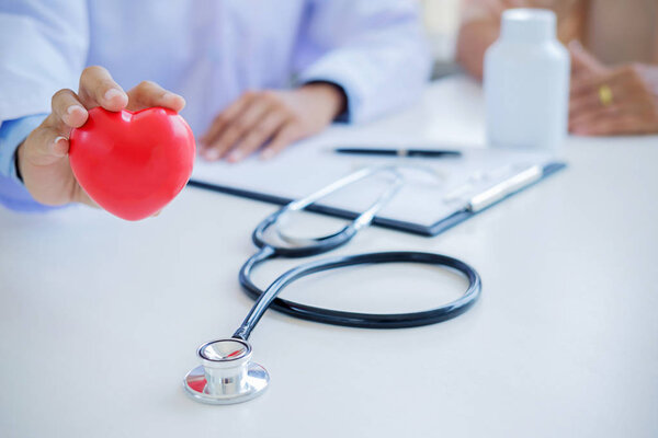 Doctor with stethoscope holding heart. Doctor and patient sitting in the room. Concept healthcare.