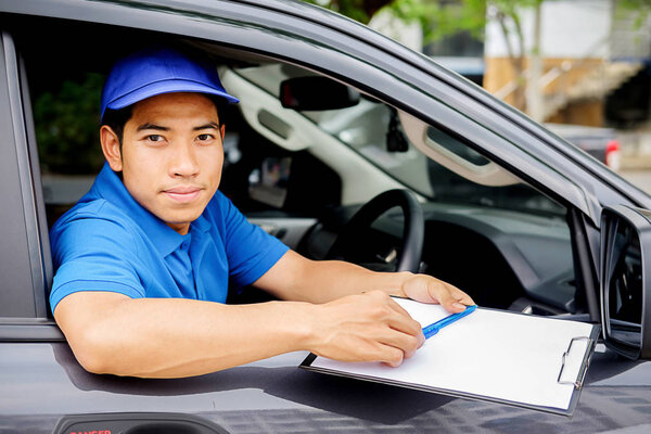 Delivery driver driving van with parcels on seat outside warehouse