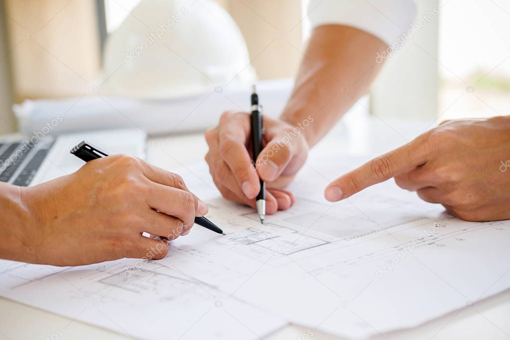 Engineers discuss a blueprint while checking information on a tablet computer in a office.