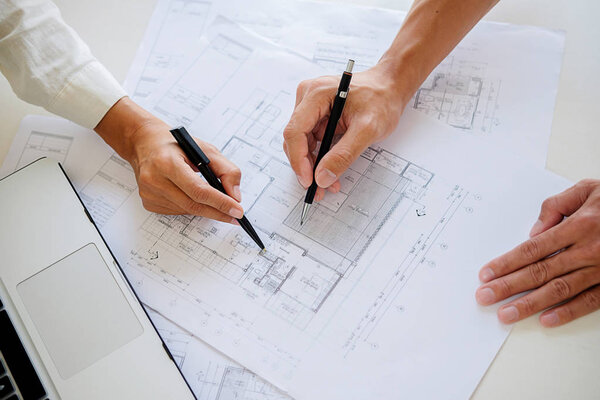 Engineers discuss a blueprint while checking information on a ta