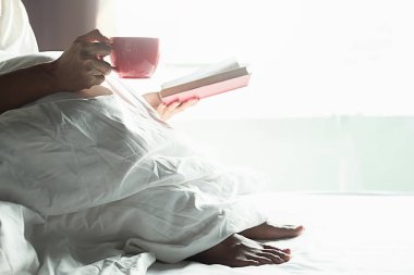 Bir fincan kahve ile yatakta oturmuş güzel Asyalı kadın. 