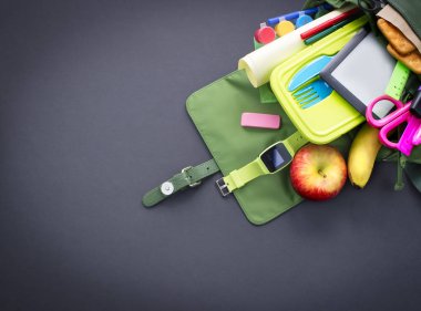 Okul malzemeleri ile siyah arka plan üzerine sırt çantası. Üstten görünüm düz yatıyordu