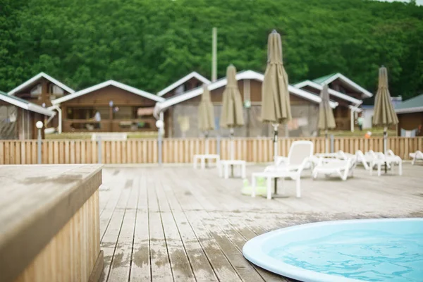Defocus blurred background recreation base wooden houses pool sunbeds wooden floor hill forest trees sky toning. Recreation center for outdoor relaxation