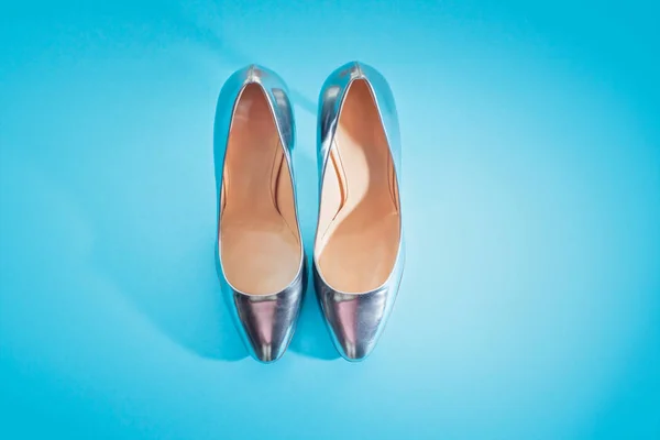 Fashionable women's shoes in silver on a blue saturated background. Top view copy space flat layer