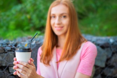 Seçici odak güzel kızıl saçlı kız bir kağıttan Kupası merdiven ve içecekler kahve gider. Park yaşam tarzı kahvaltı