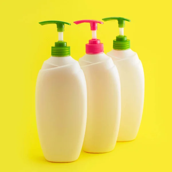 Drie plastic flessen met dispenser op gele achtergrond. — Stockfoto
