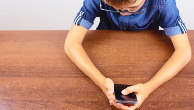 Beyaz bir arka plan Modern mobil ve iletişim üzerinde okulda masada bir cep telefonu kullanarak bir çocuğun Banner Eller