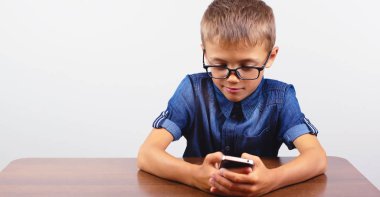 Beyaz arka plan Modern mobil ve iletişim okul Masası üzerinde cep telefonu kullanarak gözlükile gülümseyen çocuk Banner Portre