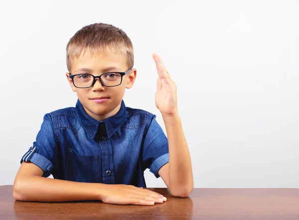 Schuljunge in blauem Hemd sitzt am Tisch. Junge mit Brille auf weißem Hintergrund zurück zur Schule — Stockfoto