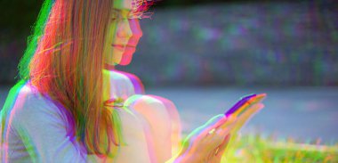 Glitch etkisi Genç güzel kız Park'ta çim üzerinde oturan cep telefonu Banner kopya alanı bakarak