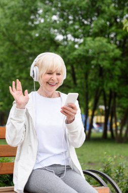 neşeli yaşlı kadın smartphone Park ve kulaklık ile müzik dinleme