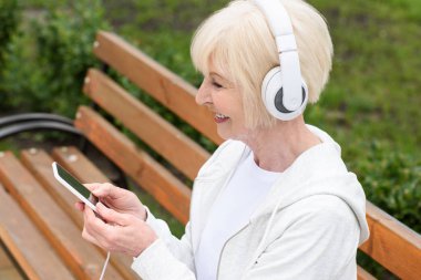 Yaşlı kadın akıllı telefon ve kulaklık ile müzik dinleme gülümseyen