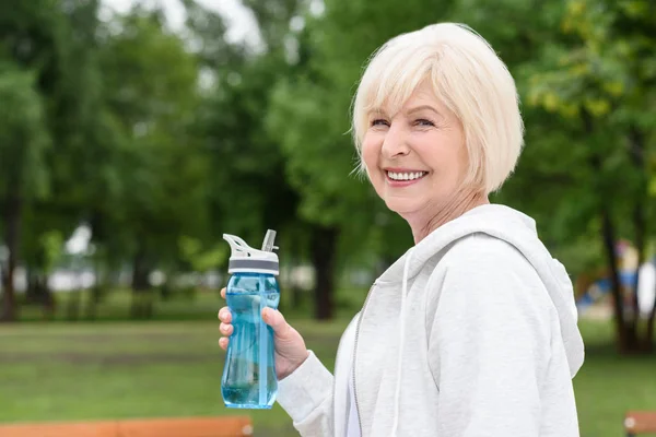 年配の女性のスポーツ ボトルを押しながらカメラに笑顔 — ストック写真