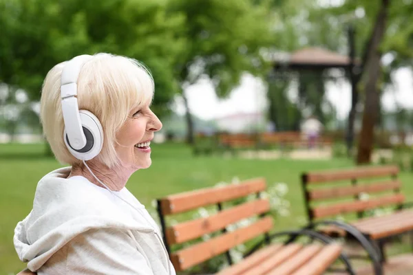 年配の女性は ヘッドフォンで音楽を聴く 公園に座っている笑顔 — ストック写真