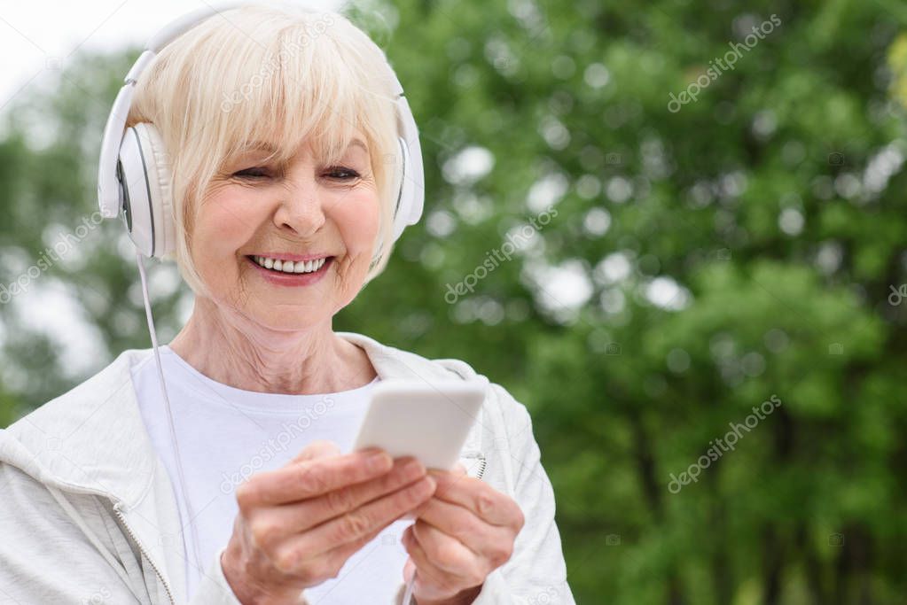 smiling senior woman using smartphone and headphones in park