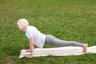 Yaşlı kadının yoga mat'ın bahçesinde tahta yapması