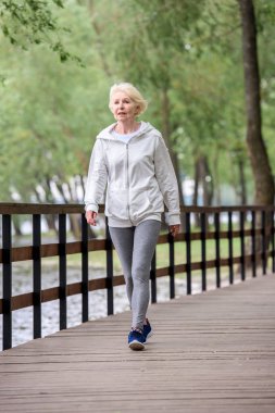 spor giyim Nehri yakınında Park ahşap yolda yürüyen kadın kıdemli