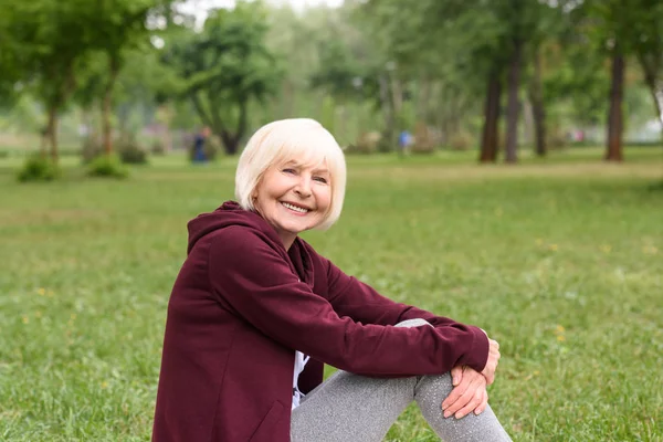 Χαρούμενα Ανώτερων Γυναίκα Που Κάθεται Στο Πράσινο Γρασίδι Στο Πάρκο — Φωτογραφία Αρχείου