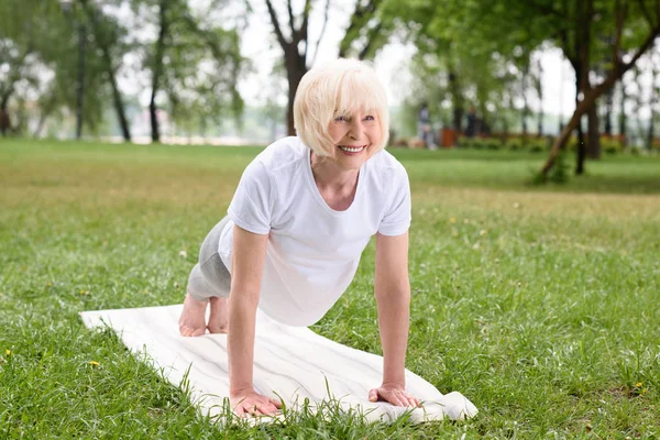 Gülümseyen Yaşlı Kadın Yoga Mat Bahçesinde Tahta Yapıyor — Stok fotoğraf