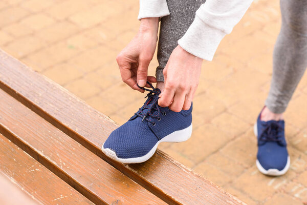 cropped view of sportswoman tying shoelaces on blue sneakers