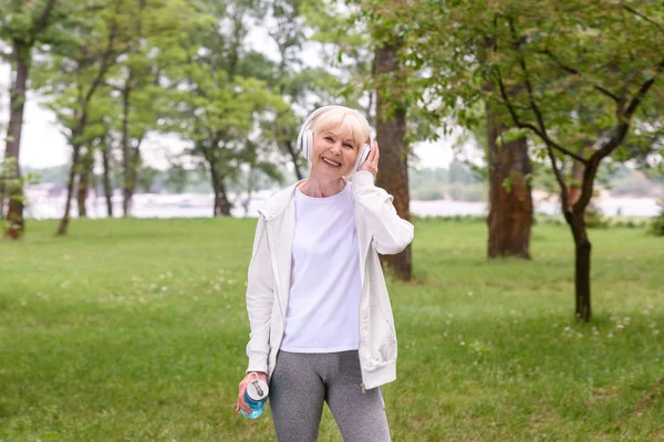 Senior Sportvrouw Met Sport Fles Luisteren Muziek Met Koptelefoon Park — Stockfoto