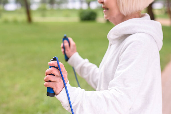cropped view of elderly sportswoman exercising with skipping rope in park