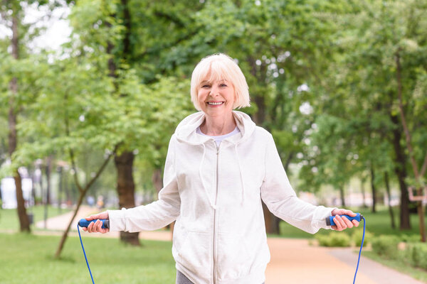 smiling elderly sportswoman with jump rope in park